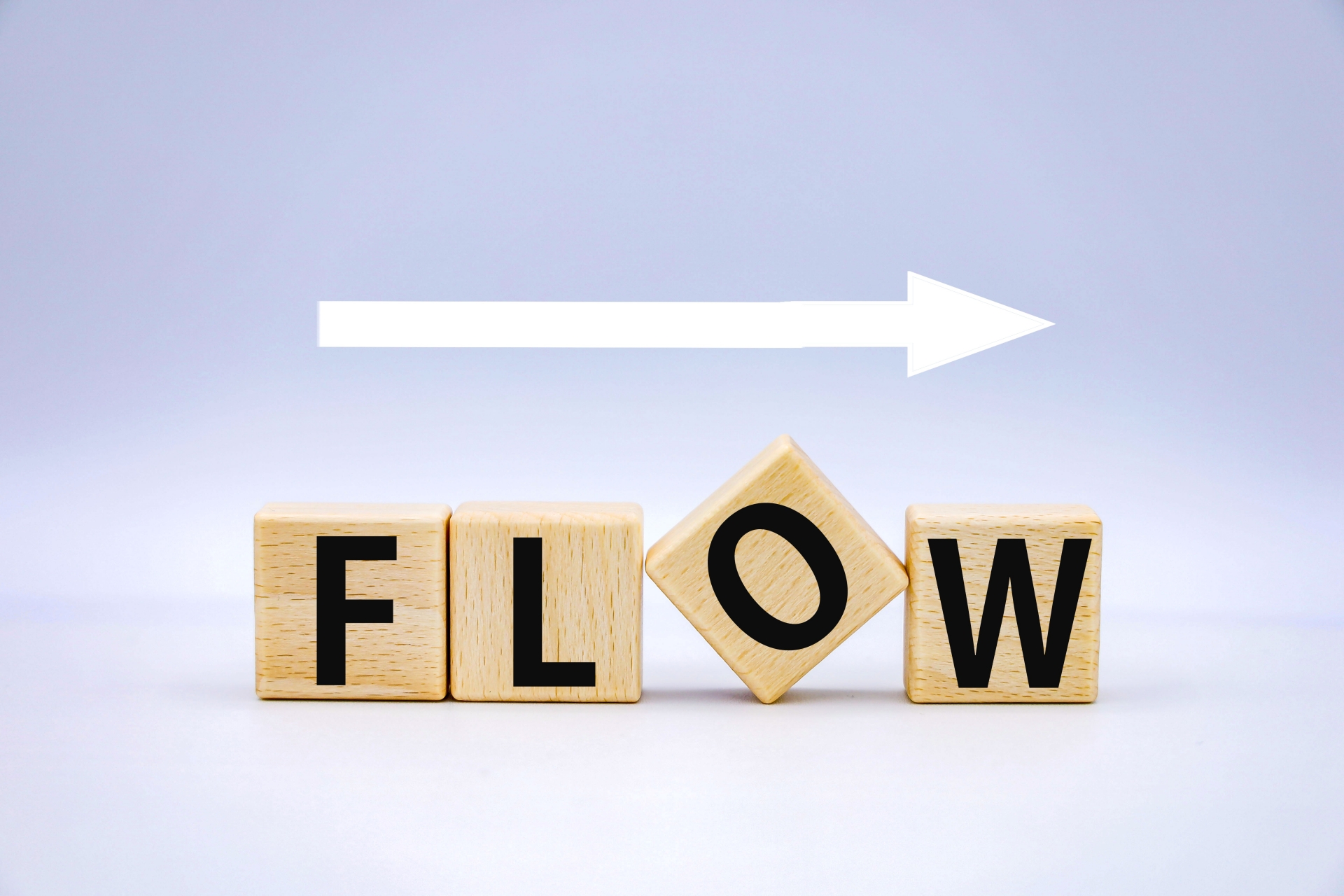 「FLOW」と書かれた木製の積み木。右向きの白い矢印が描かれている。