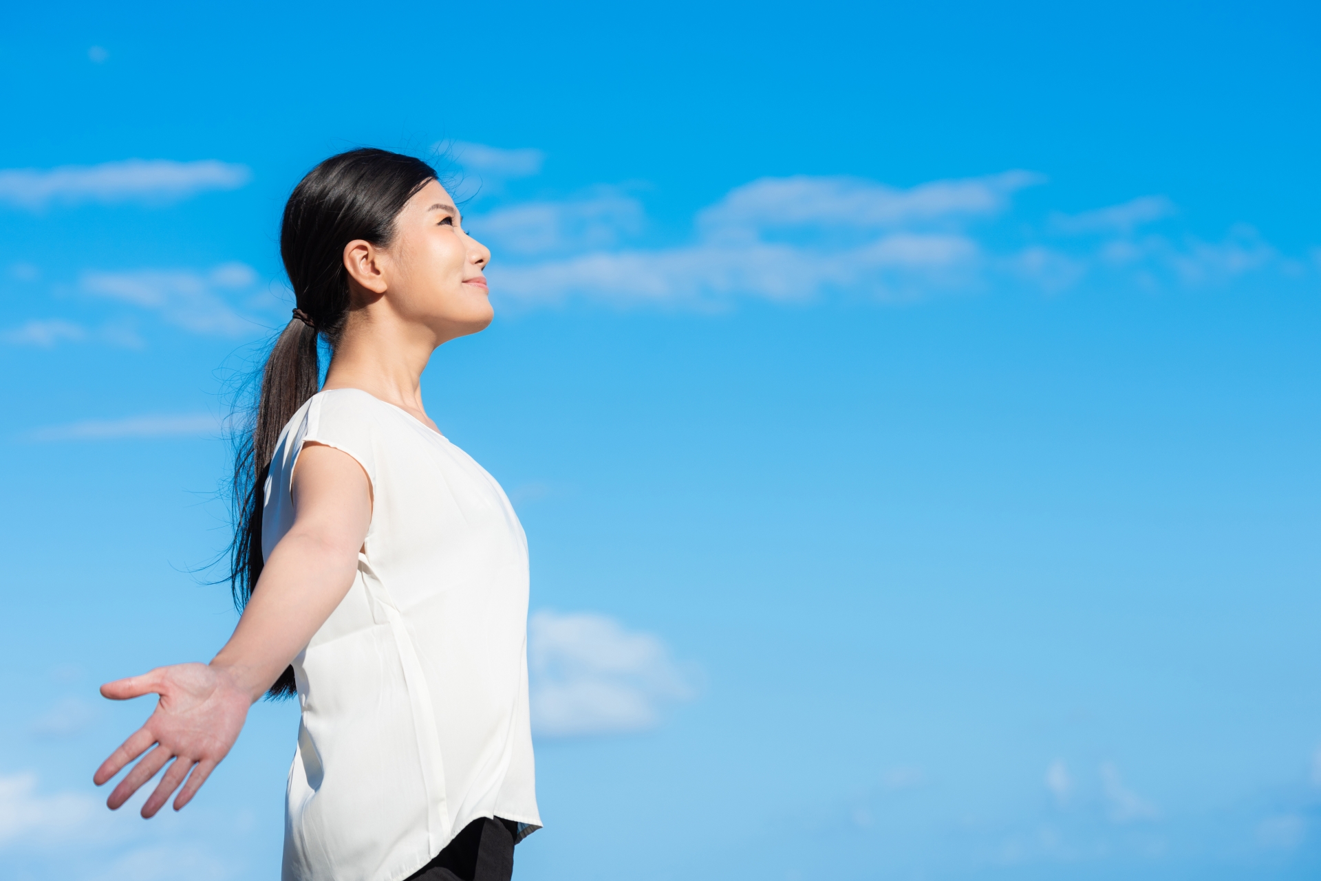 晴れた空の下で両手を広げて深呼吸する女性の画像