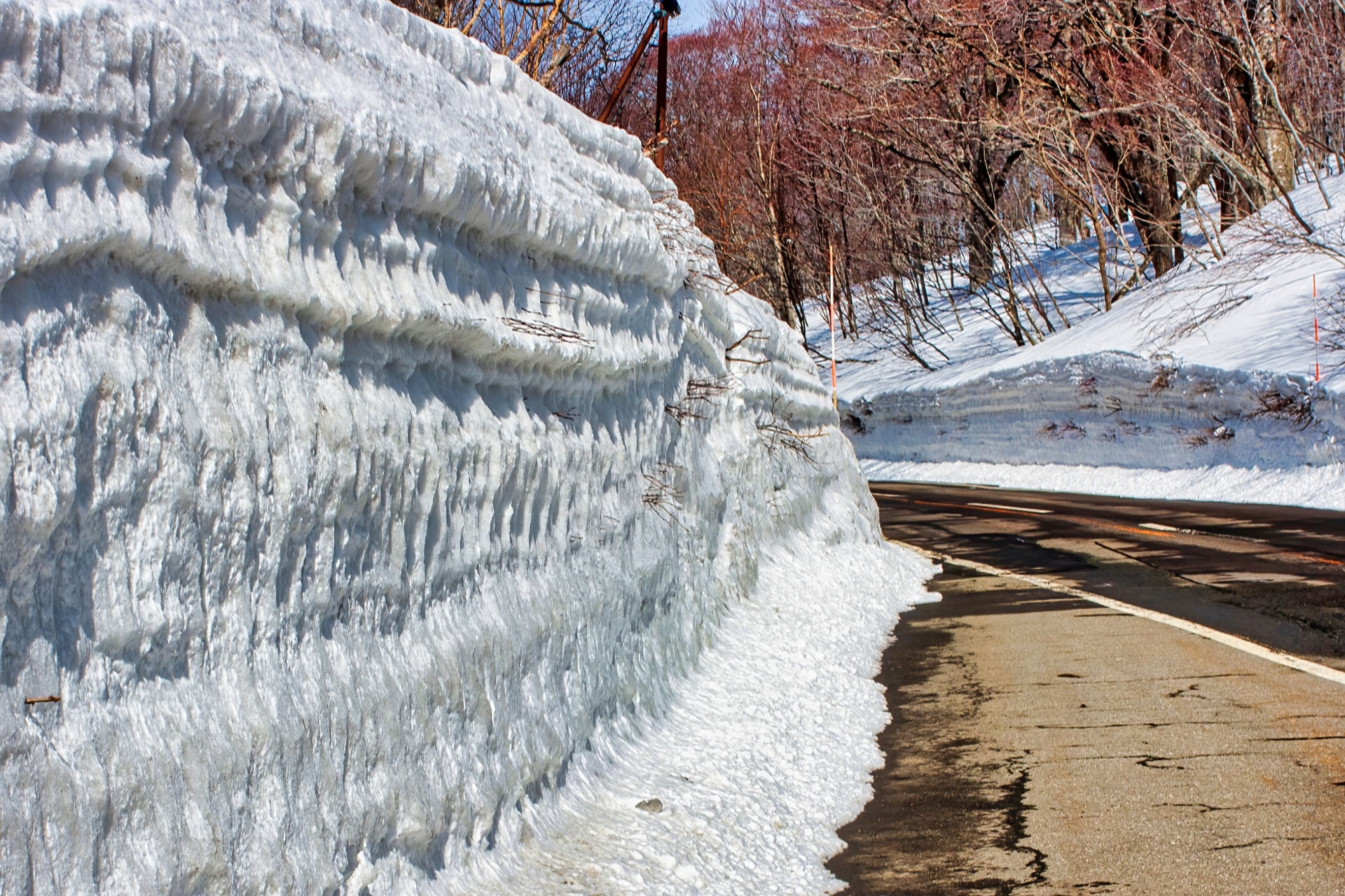 道の横に切り立った崖のように積まれる雪の壁、春の十和田八幡平 (鹿角市)
