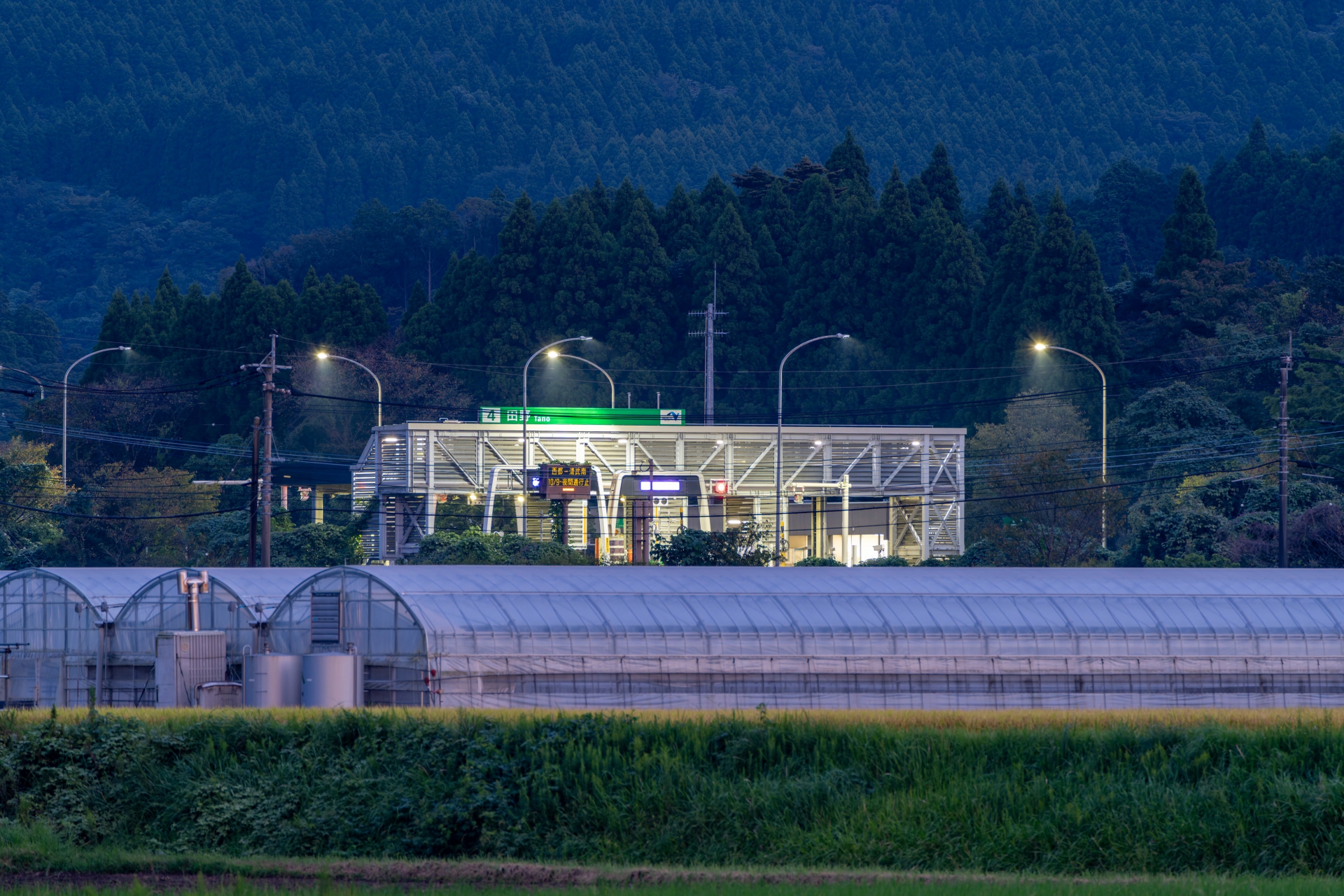 高速道路の沿線に広がる宮崎県の施設園芸用ビニールハウス群と夜間の田野料金所